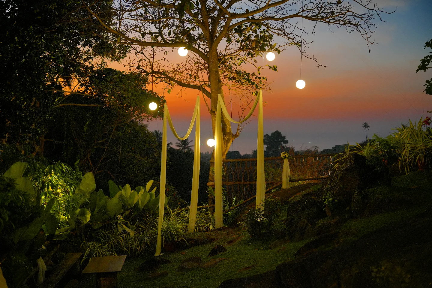 The events garden at dusk, globe lights hanging from the trees and the Arabian Sea beyond