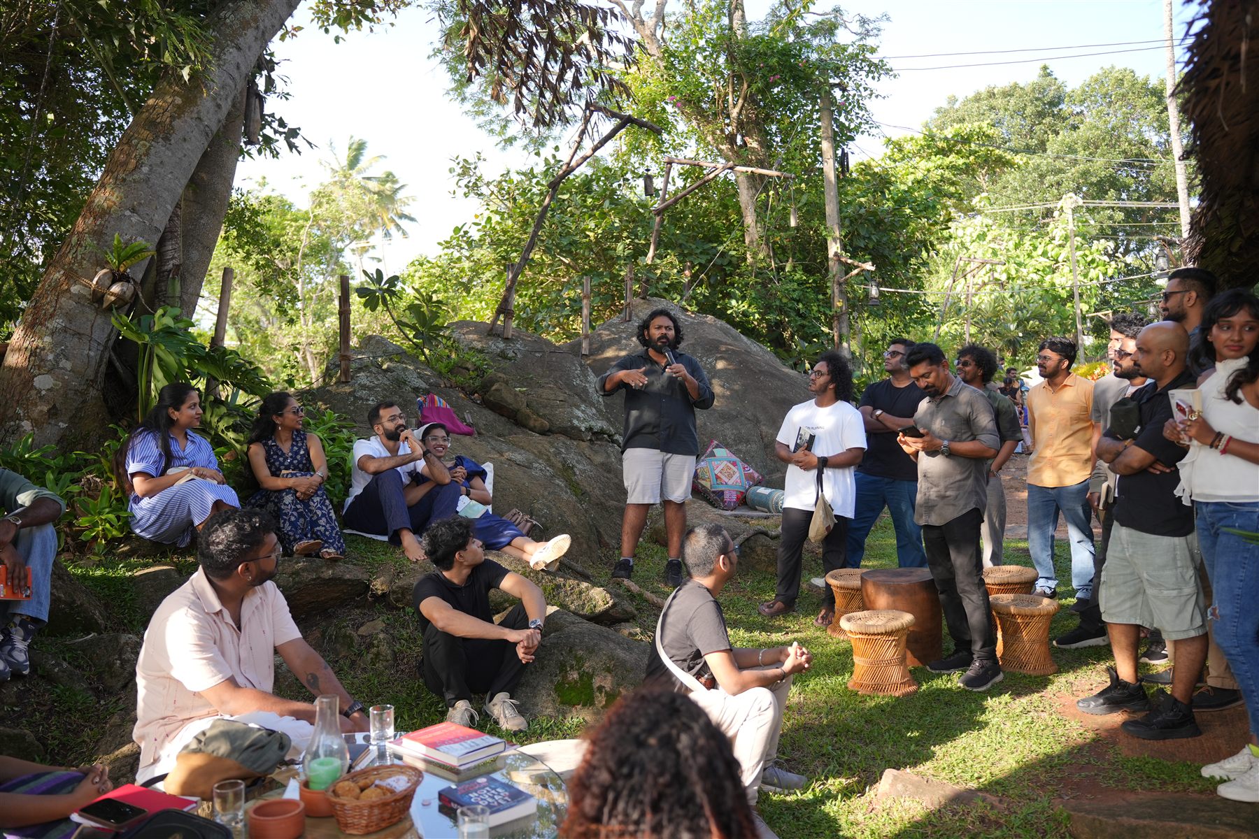 A speaker addressing a seated audience on the rocks and grass in the garden